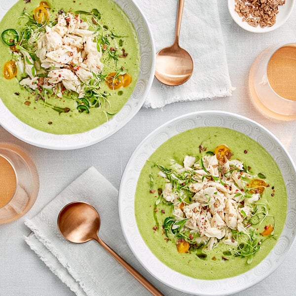 A bowl of green soup with Chesapeake Crab Connection jumbo lump blue crab meat and vegetables on a white background.