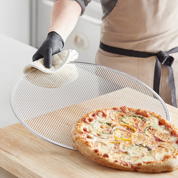 A person holding a pizza on a Choice aluminum pizza screen.