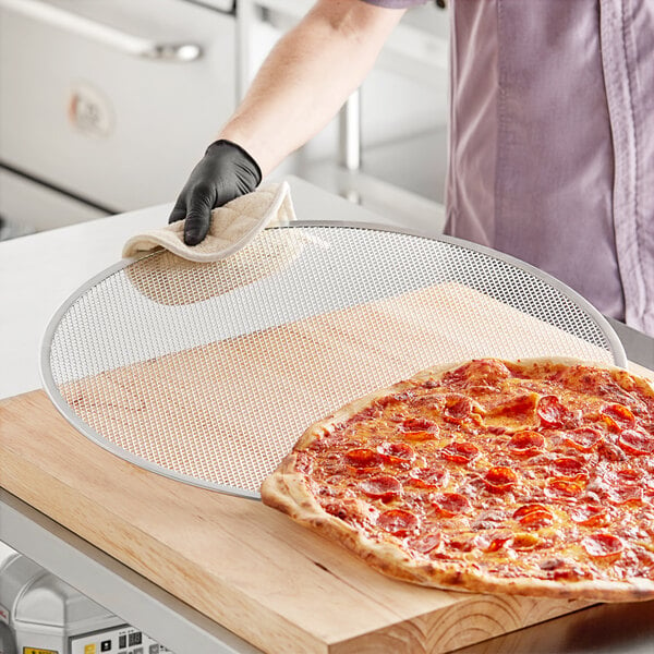 A person holding a pepperoni pizza on a Choice 22" Aluminum Pizza Screen.