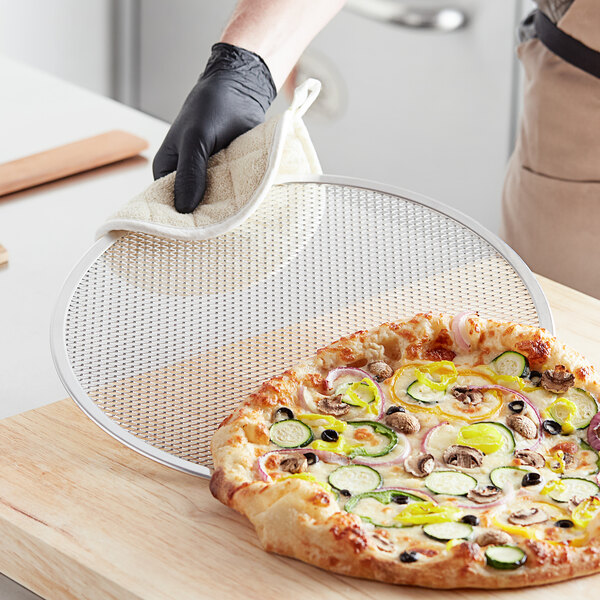 A gloved hand holding a pizza on a Choice 15" Aluminum Pizza Screen.