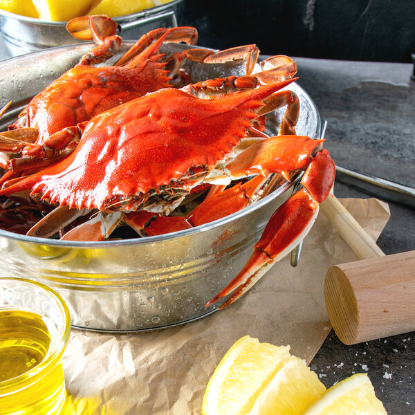 A bowl of Chesapeake blue crabs with lemons and a wooden hammer.