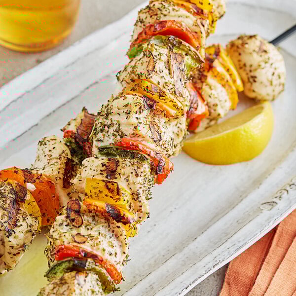 A skewer of Regal Greek Seasoned chicken and vegetables on a white plate with a lemon wedge.