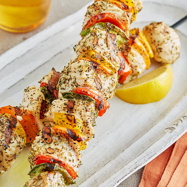 A white plate with chicken and vegetable skewers seasoned with Regal Greek Seasoning and a lemon wedge.