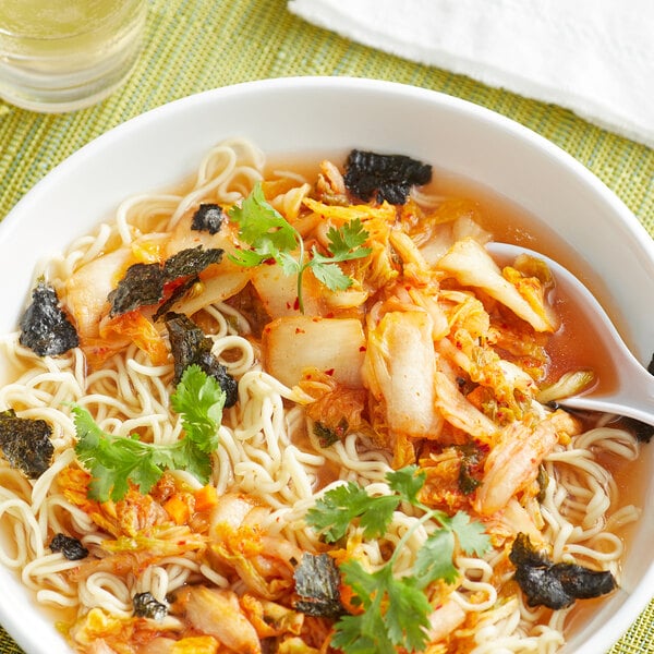 A bowl of Lucky Foods Original Kimchi soup with noodles and vegetables and a spoon.