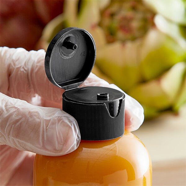 A hand holding a plastic bottle with a black flip top lid.