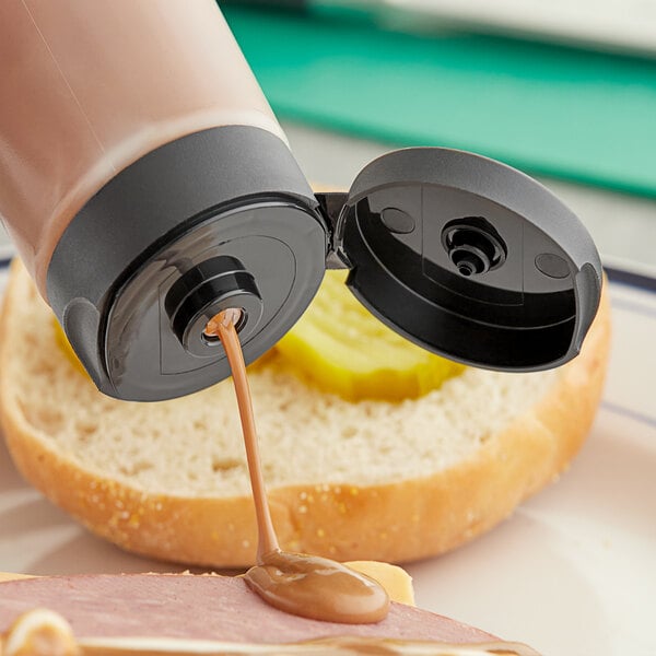 A bottle of sauce pouring into a sandwich using a black squeeze bottle lid.