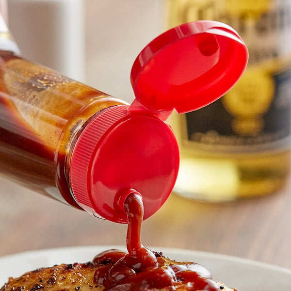 A red sauce being poured onto a piece of meat from a bottle with a red 38/400 dispensing cap.