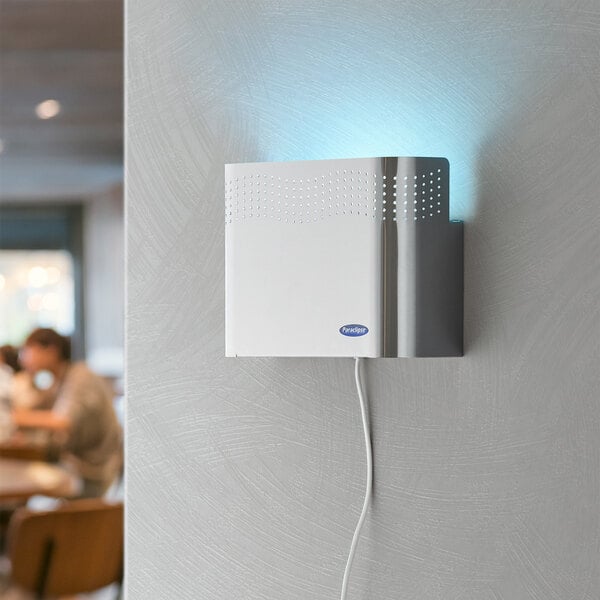A stainless steel Paraclipse Fruit Fly Patrol insect trap with a blue light on a white wall.