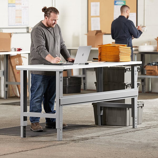 A person using a laptop on a white Lavex heavy-duty workbench top.