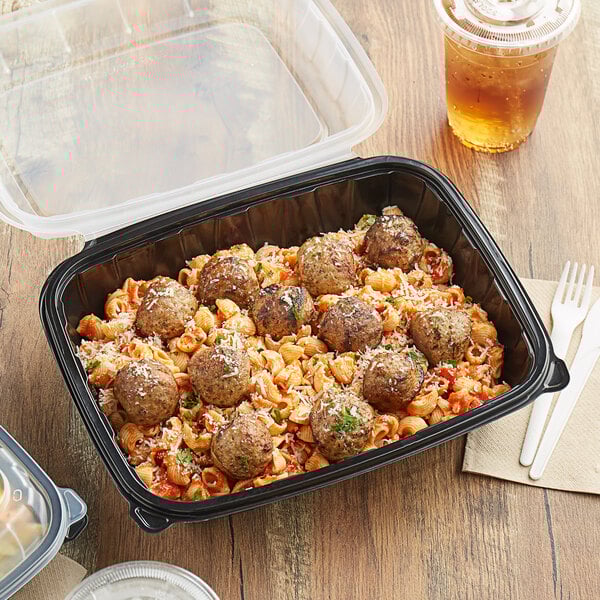 A black plastic Choice container of meatballs and pasta on a table.
