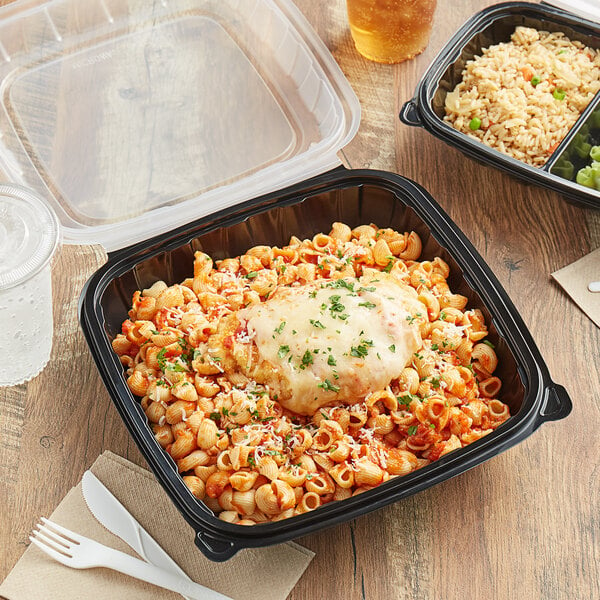 A black plastic hinged container with pasta and cheese on top on a table.