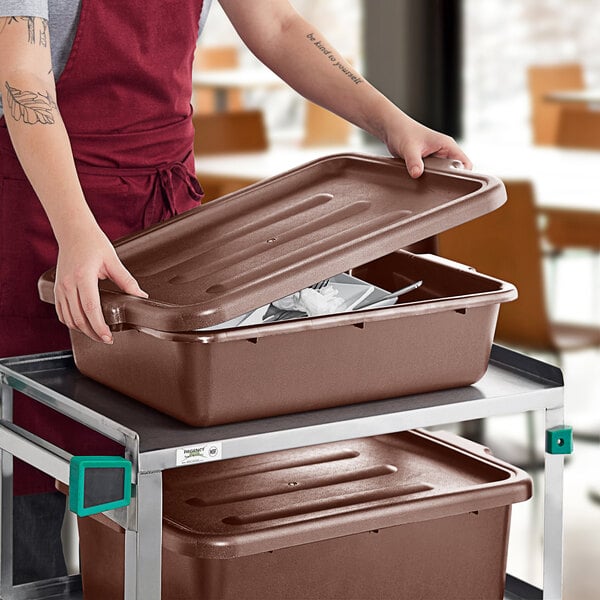 A woman putting a lid on a brown polypropylene bus tub.