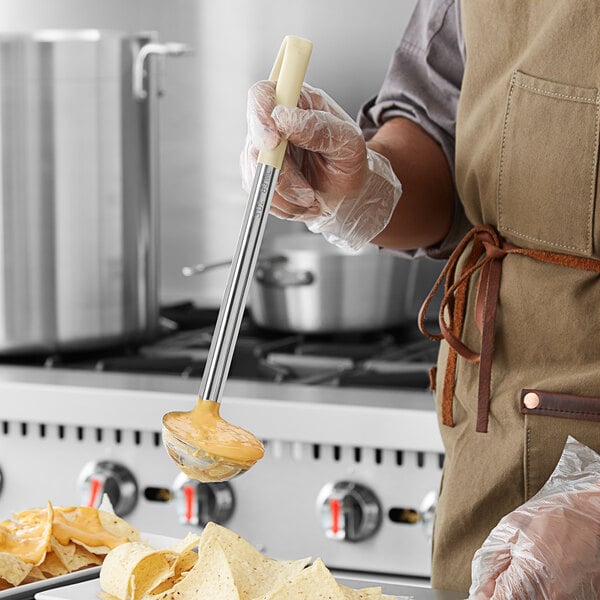 A person using a Choice stainless steel ladle with an ivory handle to pour sauce over a plate of food.