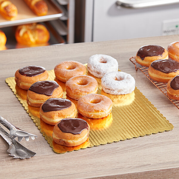 A table with a tray of chocolate covered doughnuts on a gold laminated cake board.