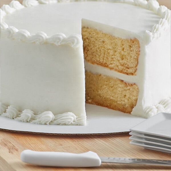 A white cake on a white 24" corrugated cake circle with a slice cut out.