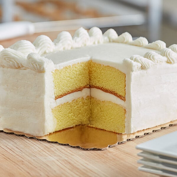 A white cake on a gold laminated cake board with two slices cut out.