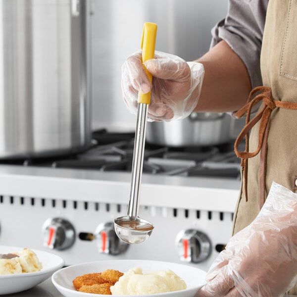 A person holding a Choice stainless steel ladle with yellow coated handle over a bowl of food.