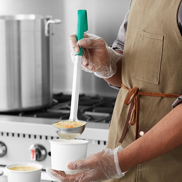 A person using a Choice stainless steel ladle with a green handle to pour soup into a white cup.