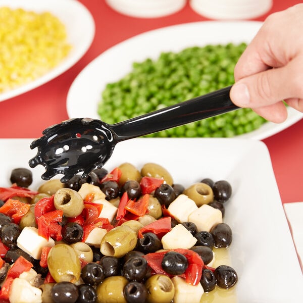 A hand using a Carlisle black pasta fork to serve food from a bowl.