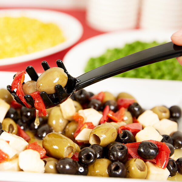 A person holding a Carlisle black pasta fork over a plate of olives and cheese.