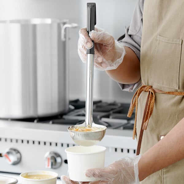 A person in a chef's uniform pouring soup with a Choice stainless steel ladle with a black handle.