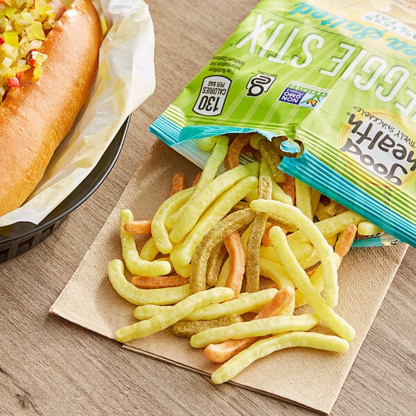 A hot dog with Sea Salted Veggie Stix and french fries on a table in a stadium concession stand.