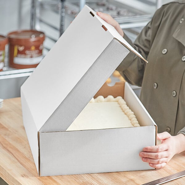 A person holding a white bakery box with a white square object in it.