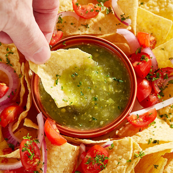 A hand dipping a chip into a bowl of tomatillo salsa.