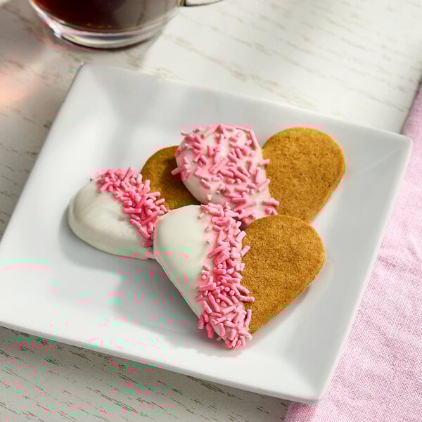 A plate of heart-shaped cookies partially dipped in white icing and decorated with pink sprinkles.