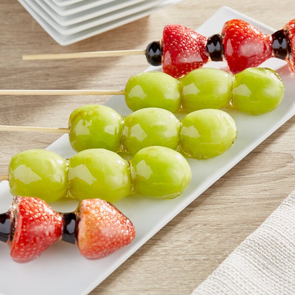 A plate of fruit on skewers with green grapes.