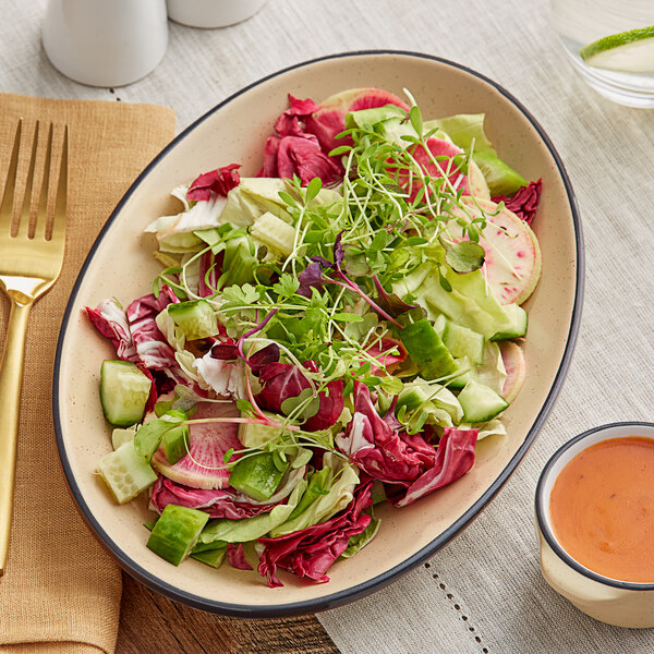 An Acopa Harvest Tan matte coupe stoneware platter with salad on a table.