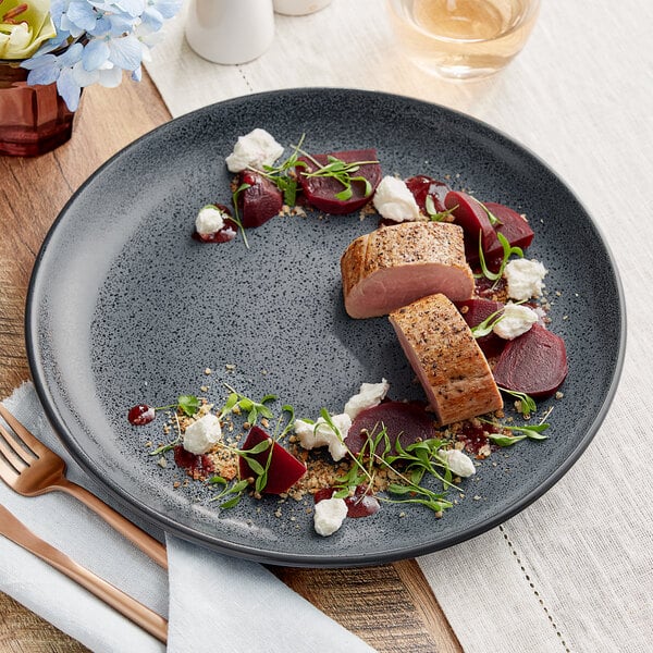 A close-up of an Acopa Embers Midnight Blue Matte Coupe stoneware plate with a piece of meat and a fork.