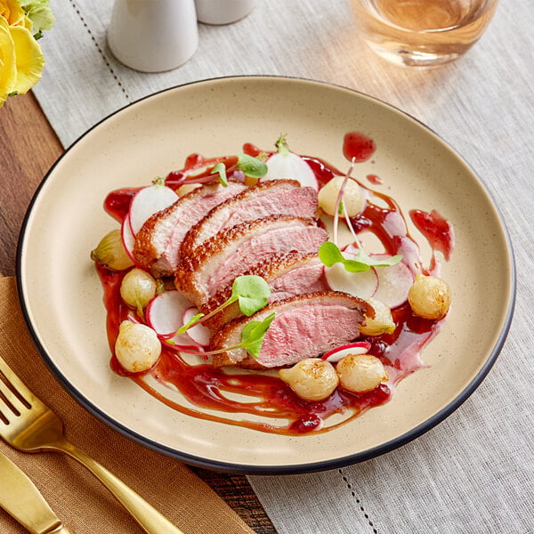 An Acopa Harvest Tan Matte coupe stoneware plate with food on it on a table.