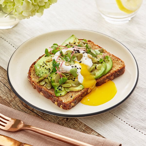 A plate of avocado toast with a poached egg on an Acopa Embers cream white matte coupe stoneware plate.