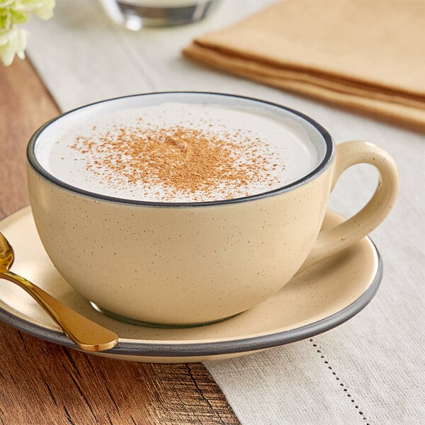 A Acopa Harvest Tan stoneware cup filled with coffee with a sprinkle of cinnamon on top.