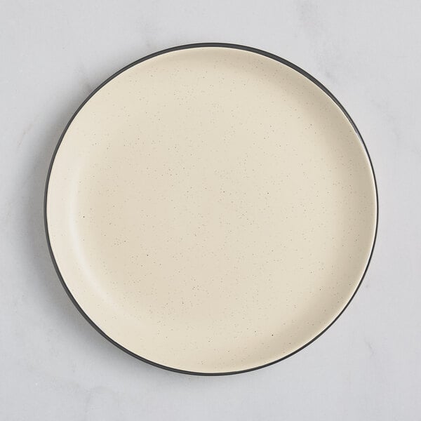An Acopa cream white stoneware plate with a black rim.