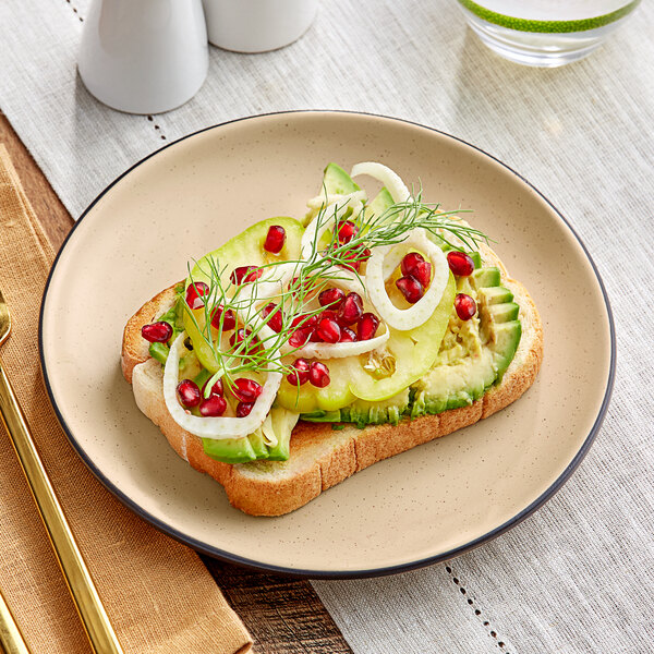 An Acopa Harvest Tan Matte Coupe stoneware plate with avocado toast, pomegranate, and red onion on a table.