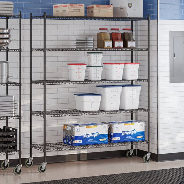A black epoxy 5-shelf wire shelving unit with casters, used for storage in a commercial kitchen.
