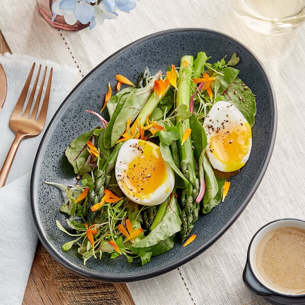 A plate of salad with eggs, greens, and vegetables served on an Acopa Midnight Blue Matte Coupe stoneware platter.