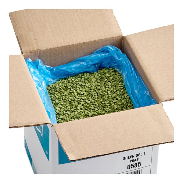 A large open cardboard box lined with a blue plastic bag and filled with dried green split peas.