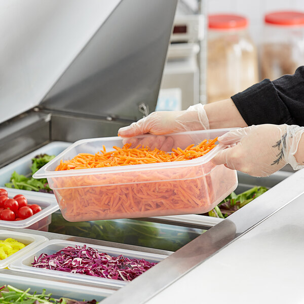 A person in gloves using a Vigor translucent polypropylene food pan to hold shredded carrots.