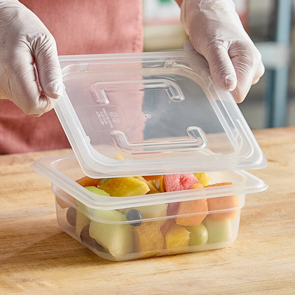 A person wearing a glove securing a Vigor translucent plastic lid on a container of fruit.