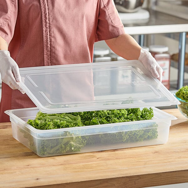 A woman in a pink shirt using a Vigor plastic container with a translucent lid to hold leafy greens.