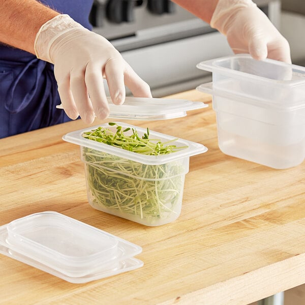 A person in gloves putting green sprouts in a Vigor translucent plastic food container.