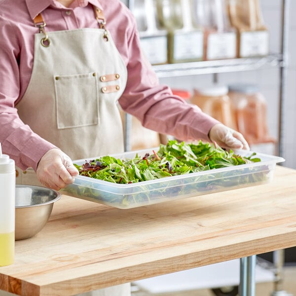 A person holding a Vigor translucent polypropylene food pan filled with salad greens.