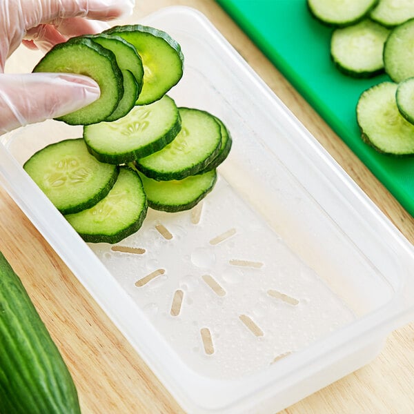 A person cutting a cucumber into a Vigor translucent polypropylene drain tray.