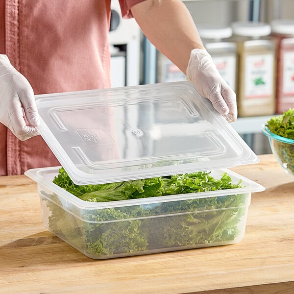 A person in gloves holding a Vigor translucent plastic container with lettuce inside.