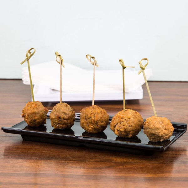 A black rectangular melamine platter with meatballs on sticks on a table.
