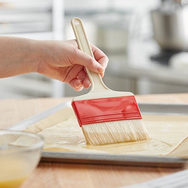 A hand holding a Choice natural bristle pastry and basting brush over a tray of dough.