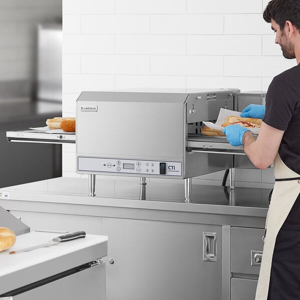 A man using a Lincoln countertop conveyor oven to make a sandwich.